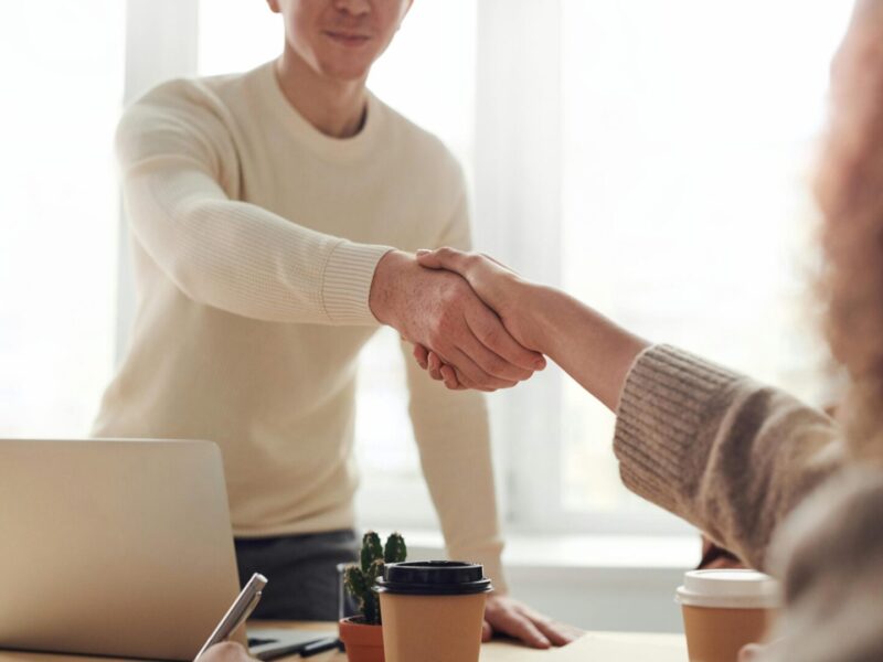 Close-up of professionals shaking hands over coffee in a modern office.